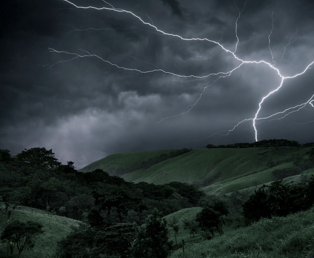 Lightning bolt striking over rolling green hills under dark storm clouds