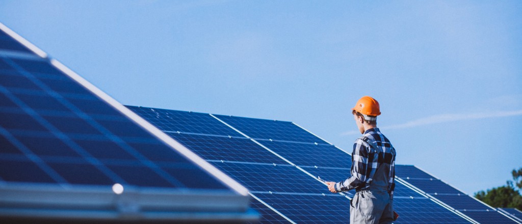 Solar energy technician inspecting photovoltaic panels under a blue sky