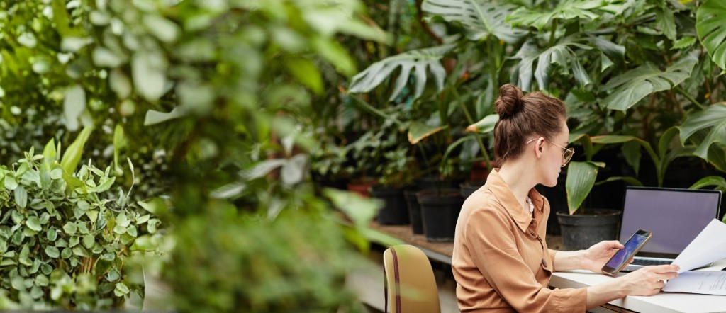 Woman working at a desk surrounded by lush indoor plants, reviewing papers and a phone